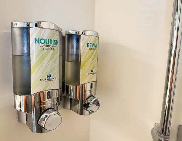 a bathroom setup on a Norwegian Cruise Line ship, featuring wall-mounted dispensers for Nourish conditioning shampoo and Revive body wash.