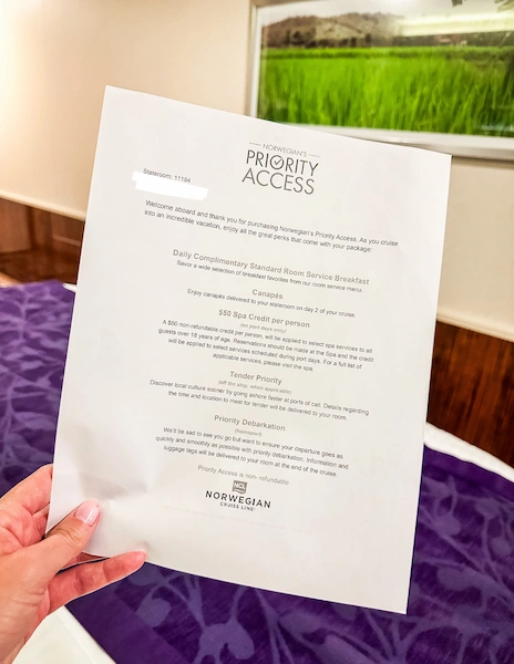 The image shows a person holding a letter detailing the benefits of Norwegian Cruise Line's Priority Access. The letter lists perks such as daily complimentary standard room service breakfast, canapés, a $50 spa credit per person, tender priority, and priority debarkation, all intended to enhance the cruise experience for guests with Priority Access.