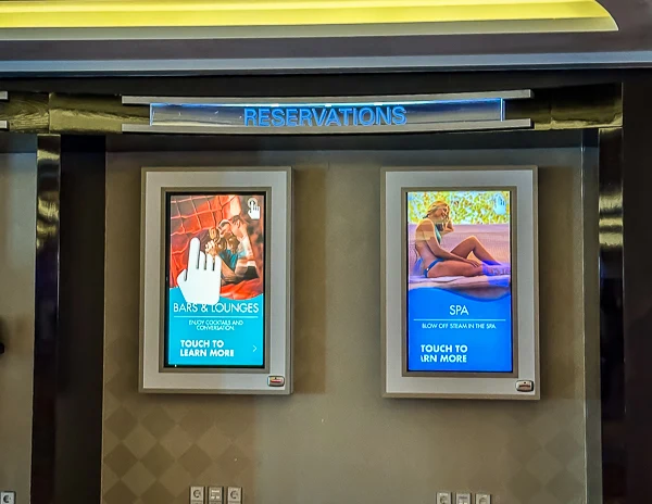 touchscreen kiosks on an NCL ship, which are used for making reservations for bars, lounges, and the spa. The screens provide an interactive and convenient way for passengers to manage their onboard activities and services.
