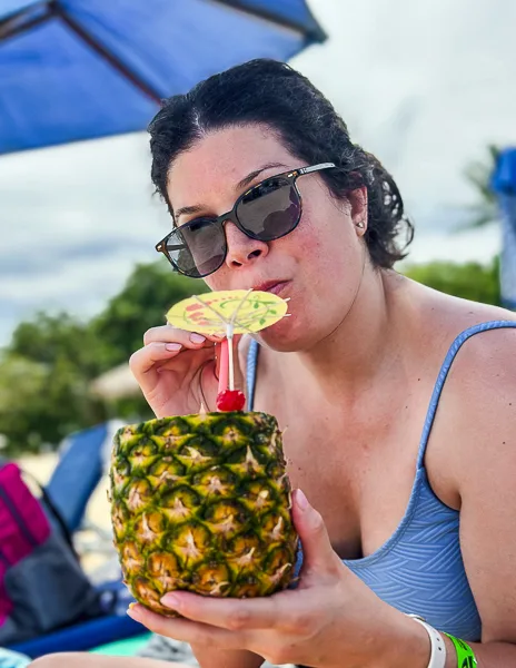 kathy (woman) drinking a piña colada served in a pineapple on the beach.