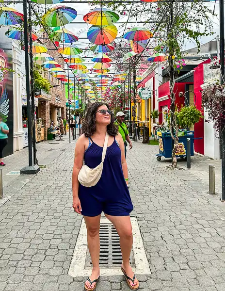 Woman (kathy) posing on Umbrella Street in Puerto Plata with colorful umbrellas overhead.