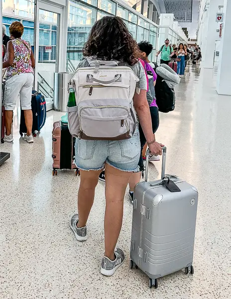 Woman (kathy) walking with a carry-on suitcase and wearing a backpack at a cruise terminal.