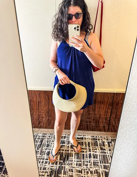 "Woman (Kathy) in a blue dress taking a mirror selfie, ready for a beach day with a sun hat and flip-flops.