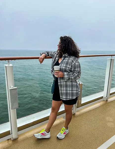 Woman (kathy) on a cruise deck in a plaid shirt, holding a coffee cup and looking out to sea on an alaska cruise.