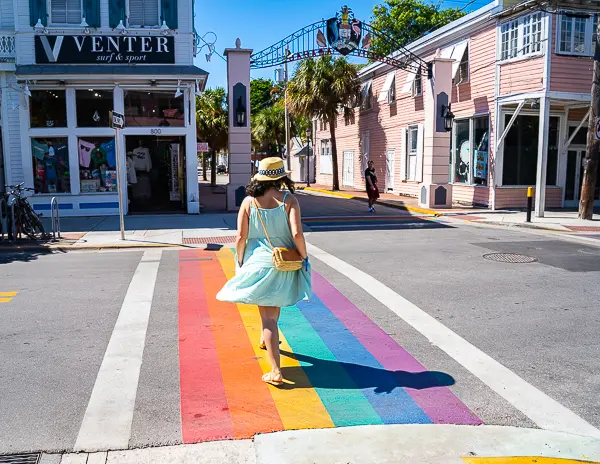 A woman (kathy) walks across a rainbow-colored crosswalk on Duval Street in Key West, highlighting the city's vibrant and inclusive atmosphere.