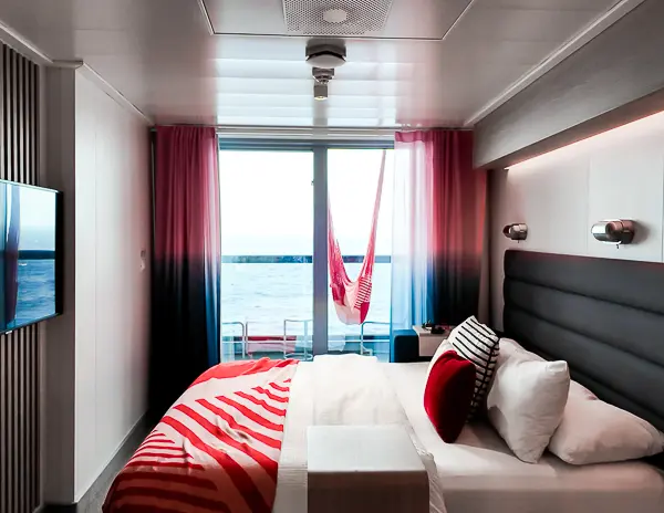 Balcony cabin on the Virgin Scarlet Lady cruise ship with a bed, hammock, and ocean view.