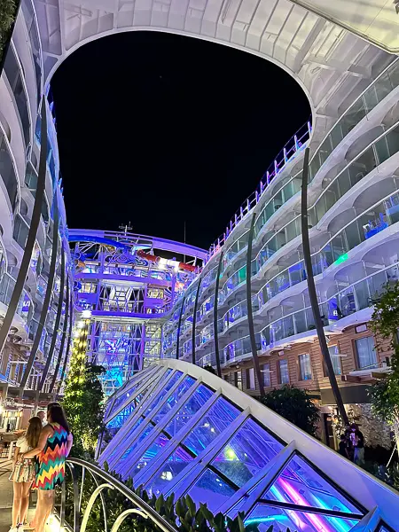 Central Park on Utopia of the Seas at night, illuminated with vibrant lights, surrounded by stateroom balconies and lush greenery, creating a lively and picturesque atmosphere.