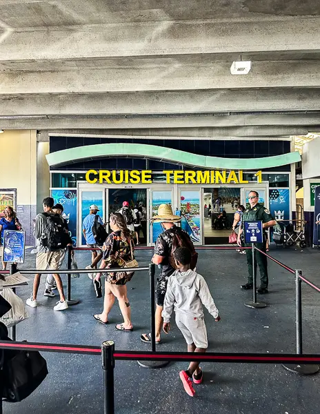 Entrance to Cruise Terminal 1 at Port Canaveral, with passengers walking toward the building, preparing to board the Utopia of the Seas.