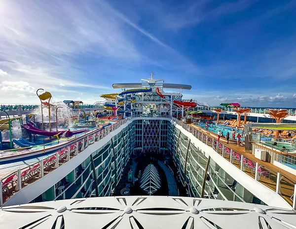 View of Deck 15 on Utopia of the Seas, featuring the water slides, splash zones, and pool areas, with passengers enjoying the sun under a clear blue sky.