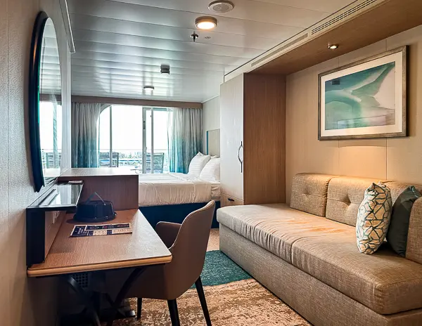 Interior of oceanview balcony cabin 9644 on Utopia of the Seas, with a bed near the balcony, a sofa, desk, and bright decor.