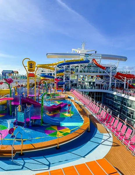 Splashaway Bay water park on Utopia of the Seas, featuring colorful slides, splash zones, and water features, with lounge chairs lining the deck under a clear blue sky.