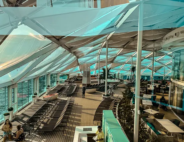 View of the Solarium on Utopia of the Seas, featuring a spacious, glass-enclosed area with lounge chairs, seating areas, and ocean views, designed for relaxation.