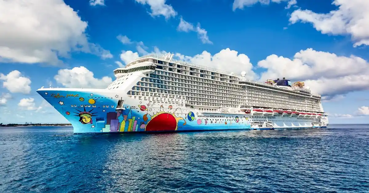 The Norwegian Breakaway cruise ship, featuring its signature colorful hull artwork, docked under a bright blue sky with scattered white clouds.