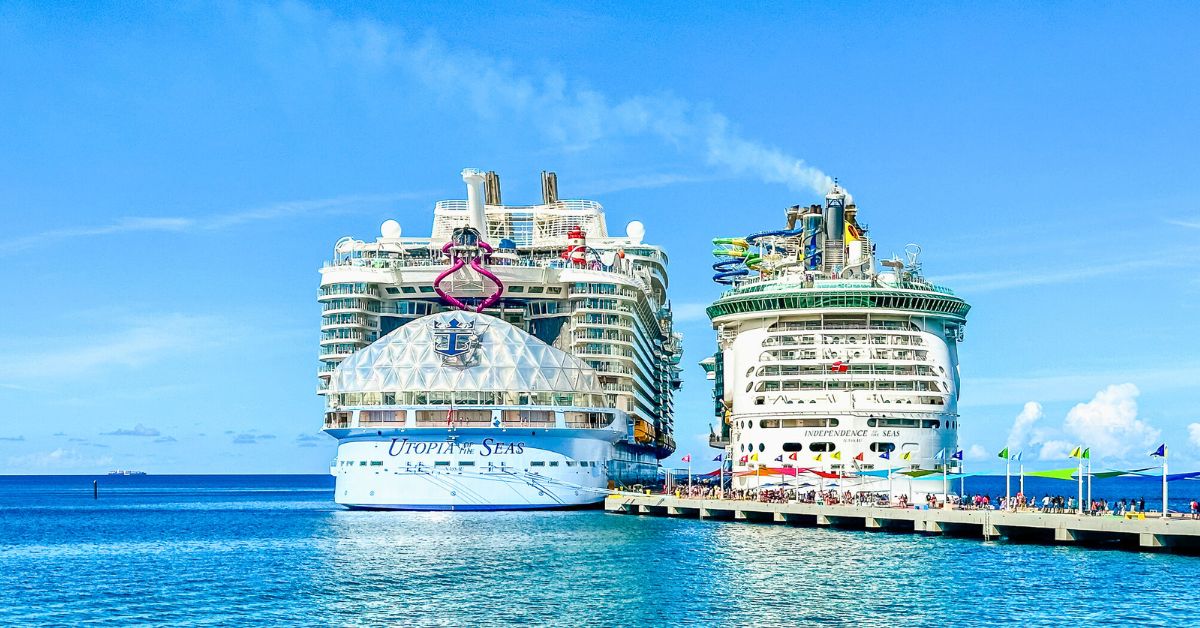 Two Royal Caribbean cruise ships, Utopia of the Seas and Independence of the Seas, docked at a sunny port with clear blue skies and calm waters, highlighting the size and features of each ship. This image pairs perfectly with Royal Caribbean cruise line tips for planning your vacation.