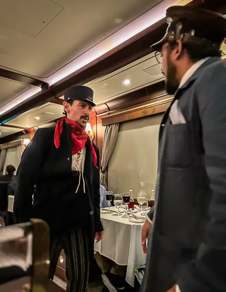 A dramatic moment between a bandit and the conductor during the Royal Railway immersive dinner show, set against the elegant train interior.