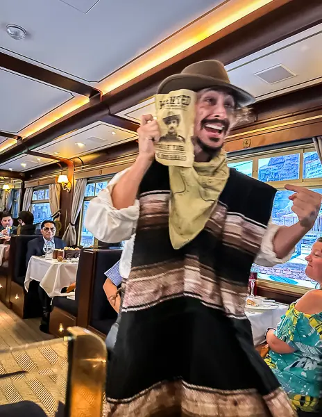 An actor dressed as a bandit during the Royal Railway dinner show, holding a "Wanted" sign and playfully interacting with guests.