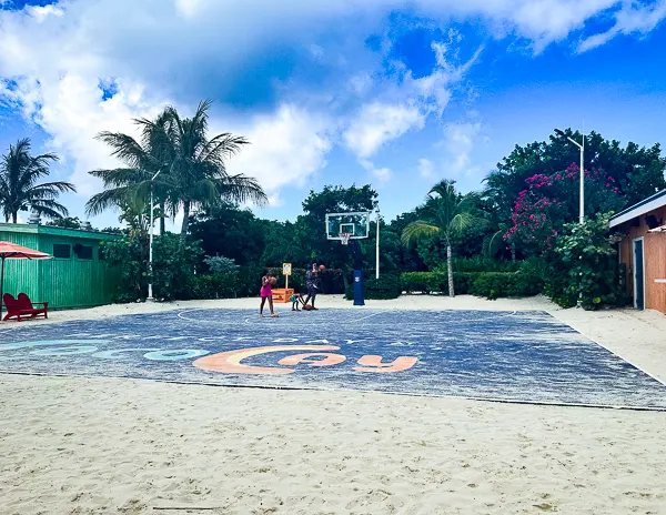 Basketball court at South Beach in CocoCay, featuring a sandy surrounding, palm trees, and a clear blue sky with guests playing a game.