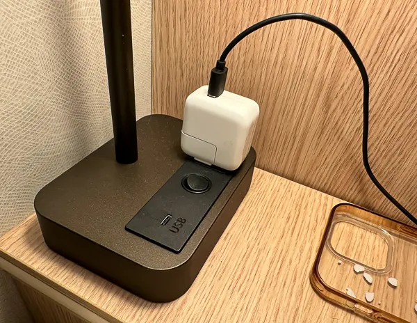 Close-up of a bedside lamp in Cabin 9644 on Utopia of the Seas, featuring a built-in USB-C port and an electrical outlet with a phone charger plugged in."