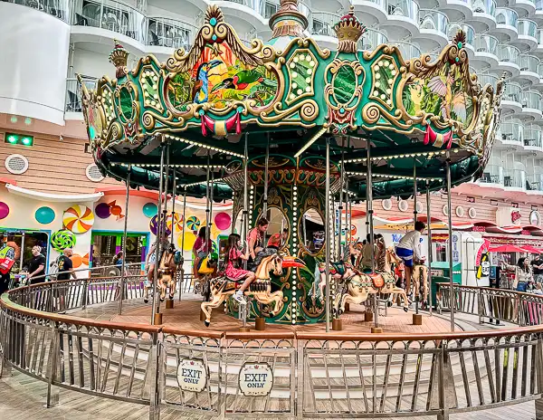 A colorful carousel on a Royal Caribbean Oasis Class ship, surrounded by bright candy-themed decor and balconies, offering a fun and whimsical activity for guests onboard.