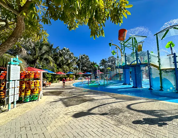 Pathway beside Splashaway Bay at CocoCay with water play areas, colorful water features, and a rack of life jackets for kids.