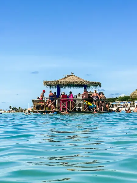 Floating bar at South Beach in CocoCay, with guests enjoying drinks under a thatched roof surrounded by calm turquoise water.