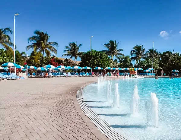 Fountains at the edge of Oasis Lagoon at CocoCay, with rows of loungers, umbrellas, and palm trees in the background.