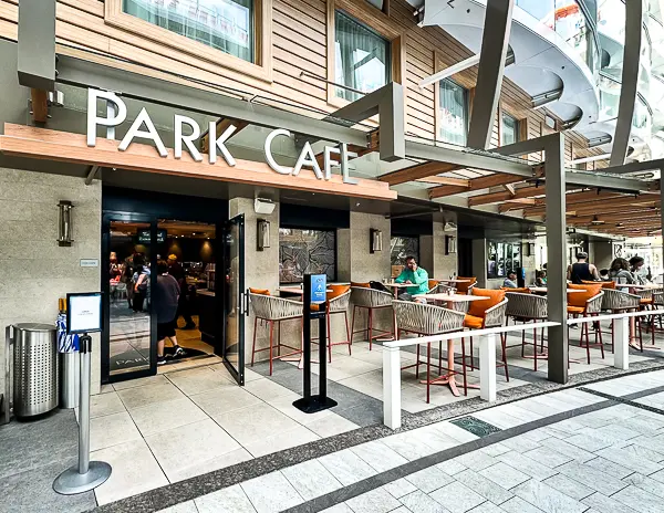 Park Cafe on Royal Caribbean’s Utopia of the Seas, featuring outdoor seating with orange chairs and a welcoming entrance where guests can grab light bites and sandwiches.