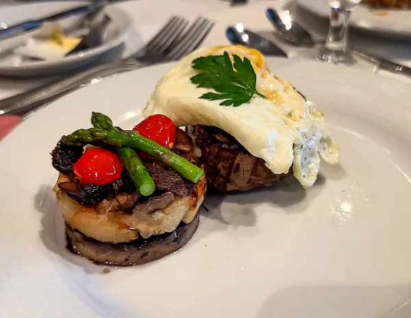 Photo of Royal Caribbean's 'The Key' breakfast dish featuring the Royal VIP Steak & Eggs, with a petite filet mignon, sautéed wild mushrooms, roasted tomatoes, asparagus, and a fried egg on top.