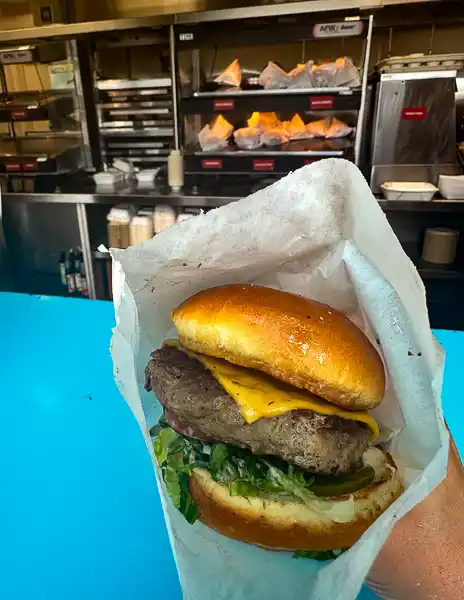 A close-up of a Shack Burger at CocoCay with a beef patty, cheese, lettuce, and pickles served on a brioche bun.