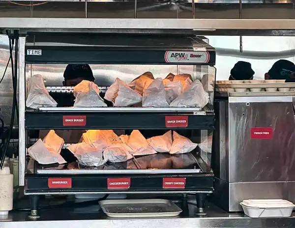 Shelves at CocoCay’s Snack Shack stocked with ready-to-go burgers, cheeseburgers, and crispy chicken sandwiches wrapped in paper.