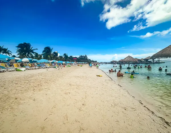 South Beach at CocoCay with rows of loungers and umbrellas lining the sandy shore, calm water, and guests swimming near in-water tables with umbrellas.