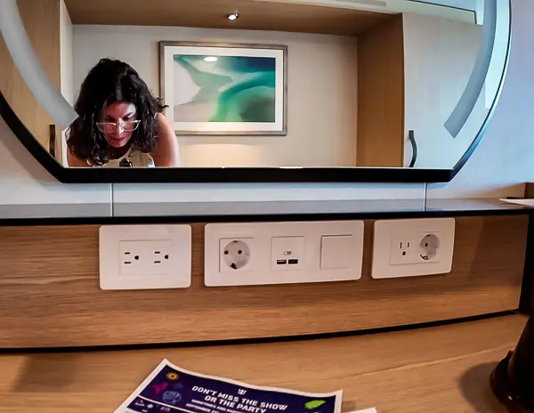 Vanity area in Cabin 9644 on Utopia of the Seas, showing multiple electrical outlets, USB-A and USB-C ports, and a guest reflected in the mirror above.