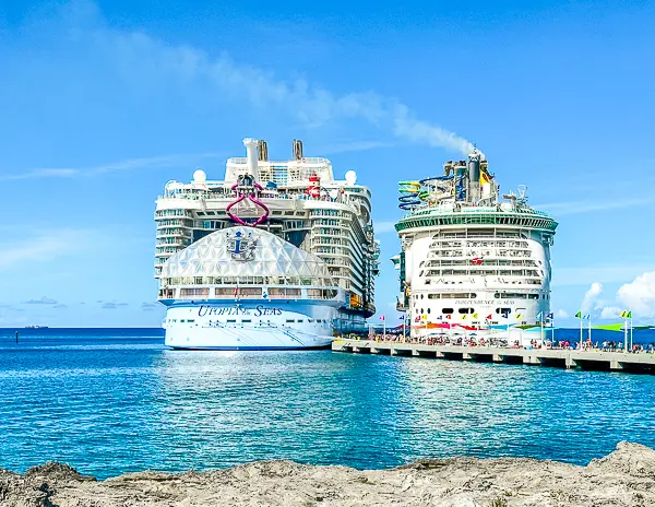 Royal Caribbean's Utopia of the Seas and Independence of the Seas docked side by side at a sunny port, showcasing their impressive size and onboard features against a clear blue sky and calm water.