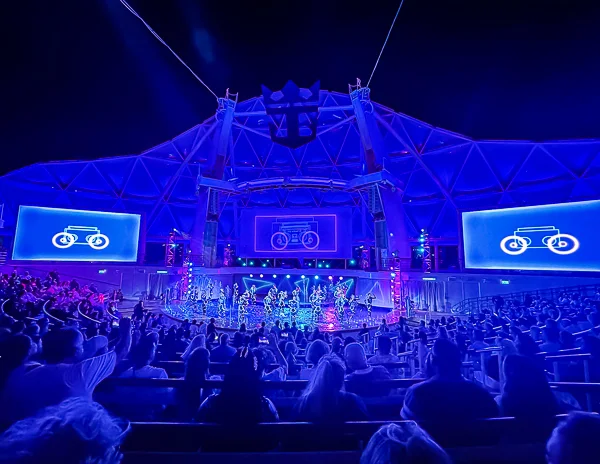 Photo of the Aqua Theater on Royal Caribbean's Utopia of the Seas during a nighttime performance, taken from The Key's reserved seating area, showcasing vibrant blue lighting and a lively crowd.