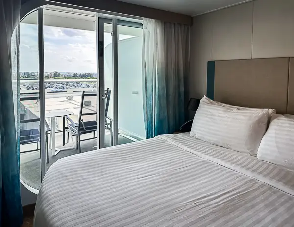 Interior view of Oceanview Balcony Cabin 9644 on Utopia of the Seas, showing a neatly made bed, sliding glass doors, and the private balcony with outdoor seating.