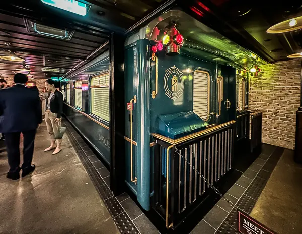 The exterior of the Royal Railway train car at Utopia Station, painted in rich blue with gold accents, glowing lanterns, and intricate details, set on a dimly lit platform.