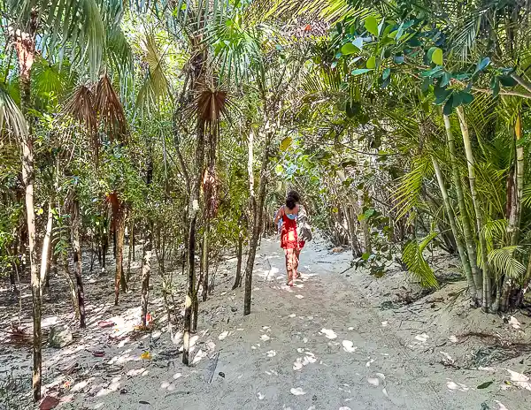 A person (kathy) walking along a sandy nature trail surrounded by lush greenery and palm trees at CocoCay.