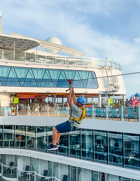 Photo of a guest (my husband) ziplining across Royal Caribbean's Utopia of the Seas, with the ship's upper deck and outdoor dining area visible in the background.