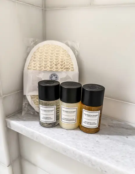 High-end shower amenities, including shampoo, conditioner, and body wash, neatly arranged on a marble shelf in the bathroom at Hotel Monteleone.