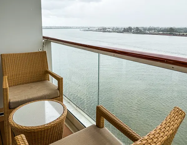 Balcony of the Norwegian Getaway Haven Penthouse Suite 14138, featuring two wicker chairs, a small table, and a view of the water.