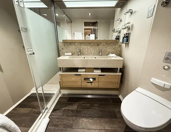 Bathroom of the Norwegian Getaway Haven Penthouse Suite 14138, showcasing a double sink vanity, glass shower, and tiled flooring.