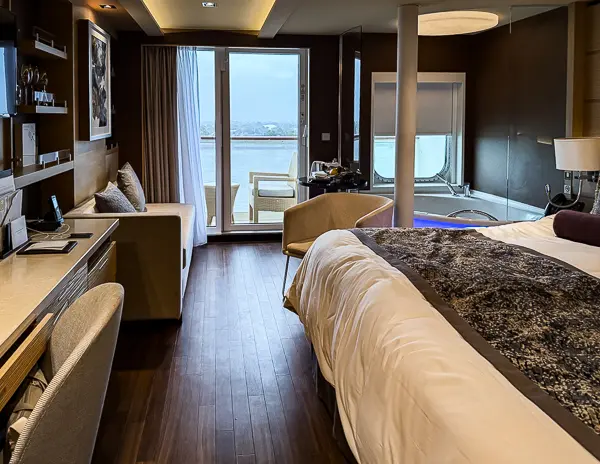 Wide shot of the Norwegian Getaway Haven Penthouse Suite 14138, showing the king-sized bed, jacuzzi, and access to the balcony.