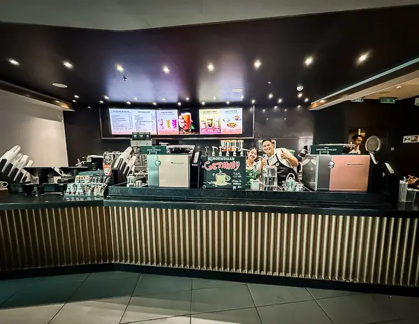 The Starbucks counter onboard the Norwegian Getaway, with baristas smiling behind the counter and the drink menu displayed above.