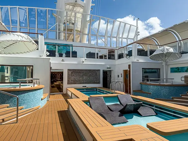 The Haven pool area on the Norwegian Getaway, featuring a private pool, hot tubs, and comfortable loungers in an upscale, semi-enclosed setting with a glass canopy and bright sunlight.