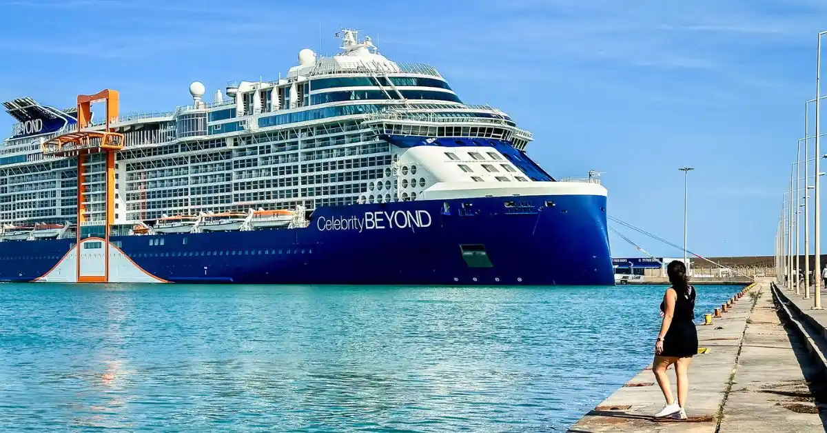 featured image: A person (kathy) standing on the dock, gazing at the Celebrity Beyond cruise ship with clear blue skies and calm water, showcasing the scale and grandeur of the ship.