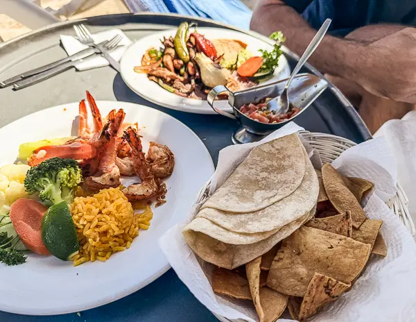 Mexican food served at Nachi Cocom Beach Club in Cozumel, featuring grilled shrimp, rice, vegetables, tortillas, chips, and salsa on an outdoor table.