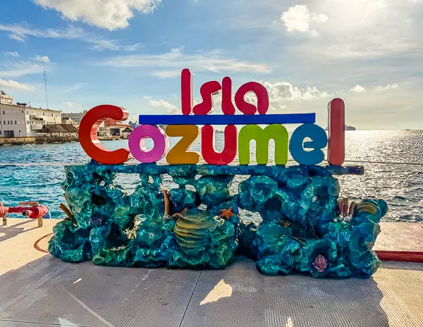 Colorful 'Isla Cozumel' sign at Punta Langosta cruise terminal, featuring a coral reef-inspired base with ocean views in the background.