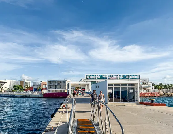 Punta Langosta cruise terminal in Cozumel, Mexico, with passengers walking along the pier toward the terminal entrance. 